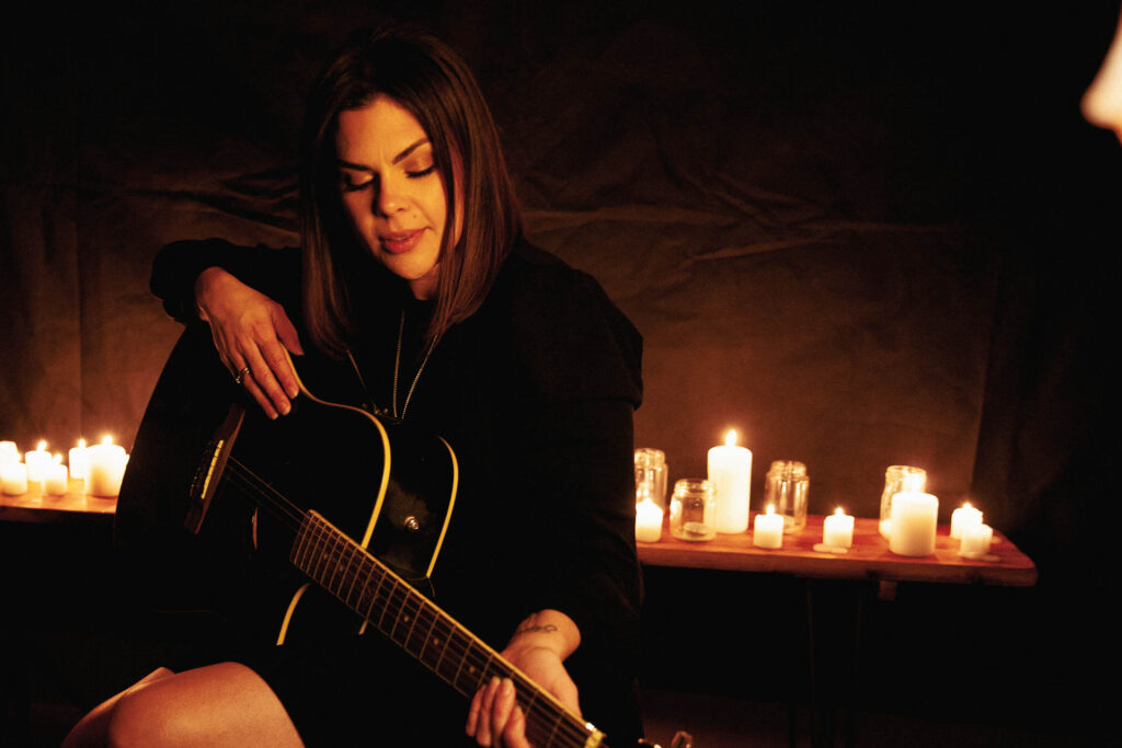 Portrait of Jessica Wishart with a guitar and candles in the background